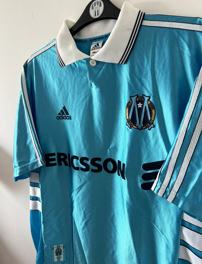 Maillot de foot vintage extérieur bleu de l'OM 1998. On peut retrouver l'équipementier Adidas et le sponsor Ericsson. Il s'agit d'un maillot authentique d'époque.