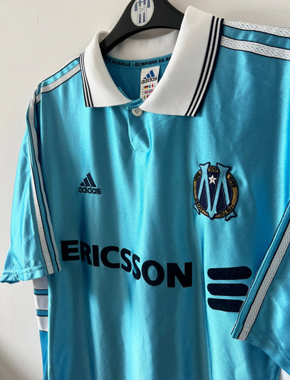 Maillot de foot vintage bleu de l'OM 1998/1999 du centenaire. On peut retrouver l'équipementier Adidas et le sponsor Ericsson. Il s'agit d'un maillot authentique d'époque.