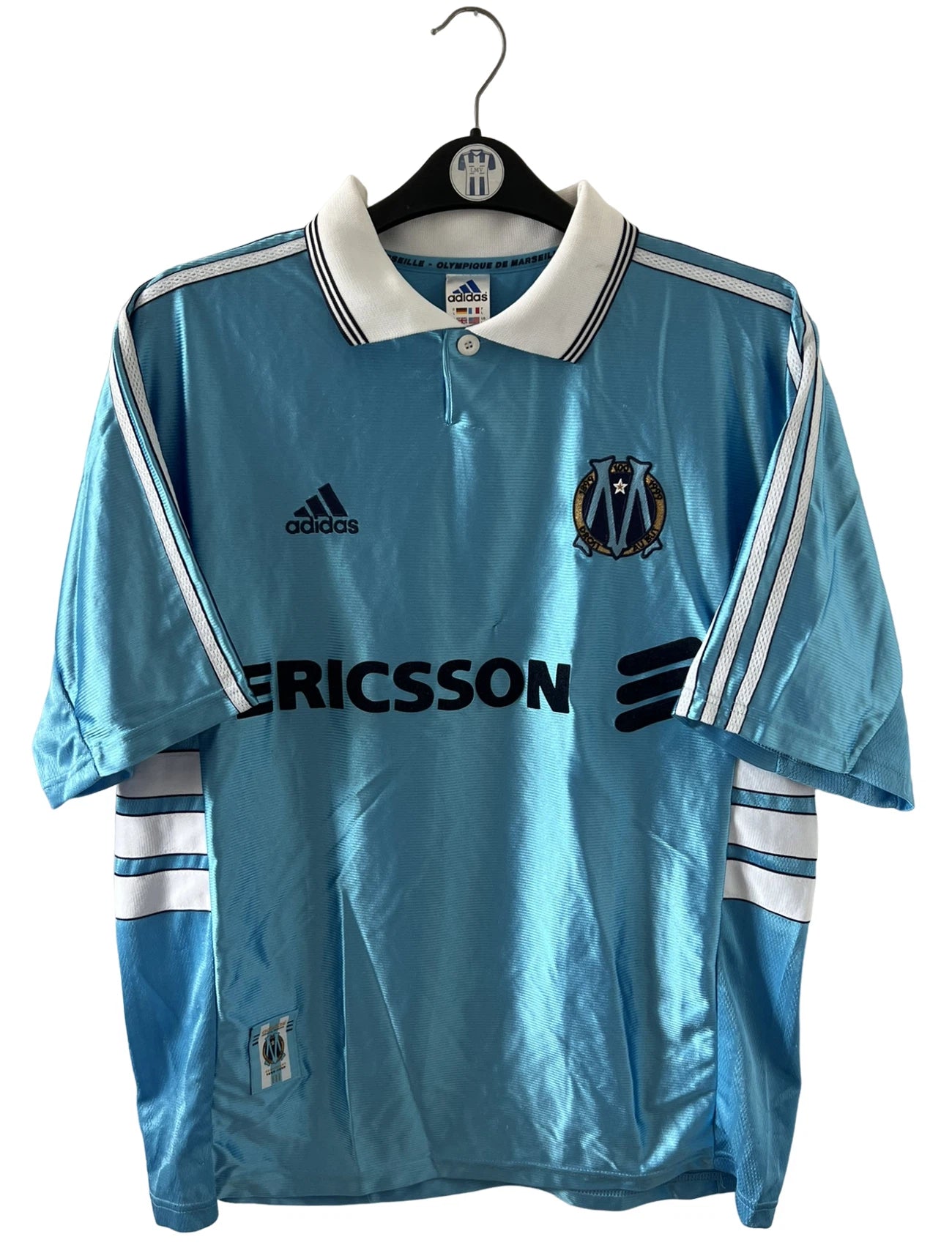 Maillot de foot vintage extérieur bleu de l'OM 1998. On peut retrouver l'équipementier Adidas et le sponsor Ericsson. Il s'agit d'un maillot authentique d'époque.