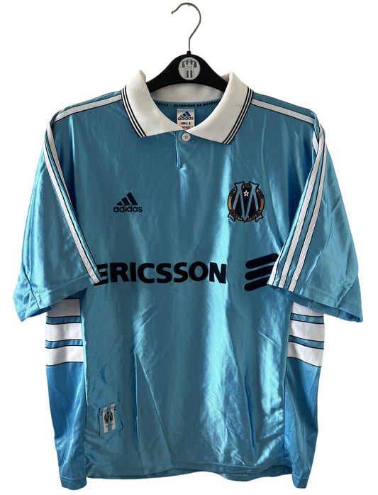 Maillot de foot vintage extérieur bleu de l'OM 1998. On peut retrouver l'équipementier Adidas et le sponsor Ericsson. Il s'agit d'un maillot authentique d'époque.