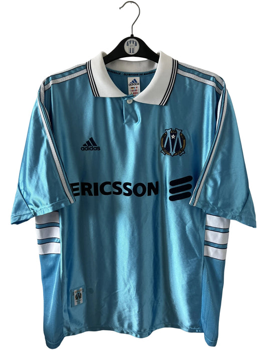 Maillot de foot vintage bleu de l'OM 1998/1999 du centenaire. On peut retrouver l'équipementier Adidas et le sponsor Ericsson. Il s'agit d'un maillot authentique d'époque.