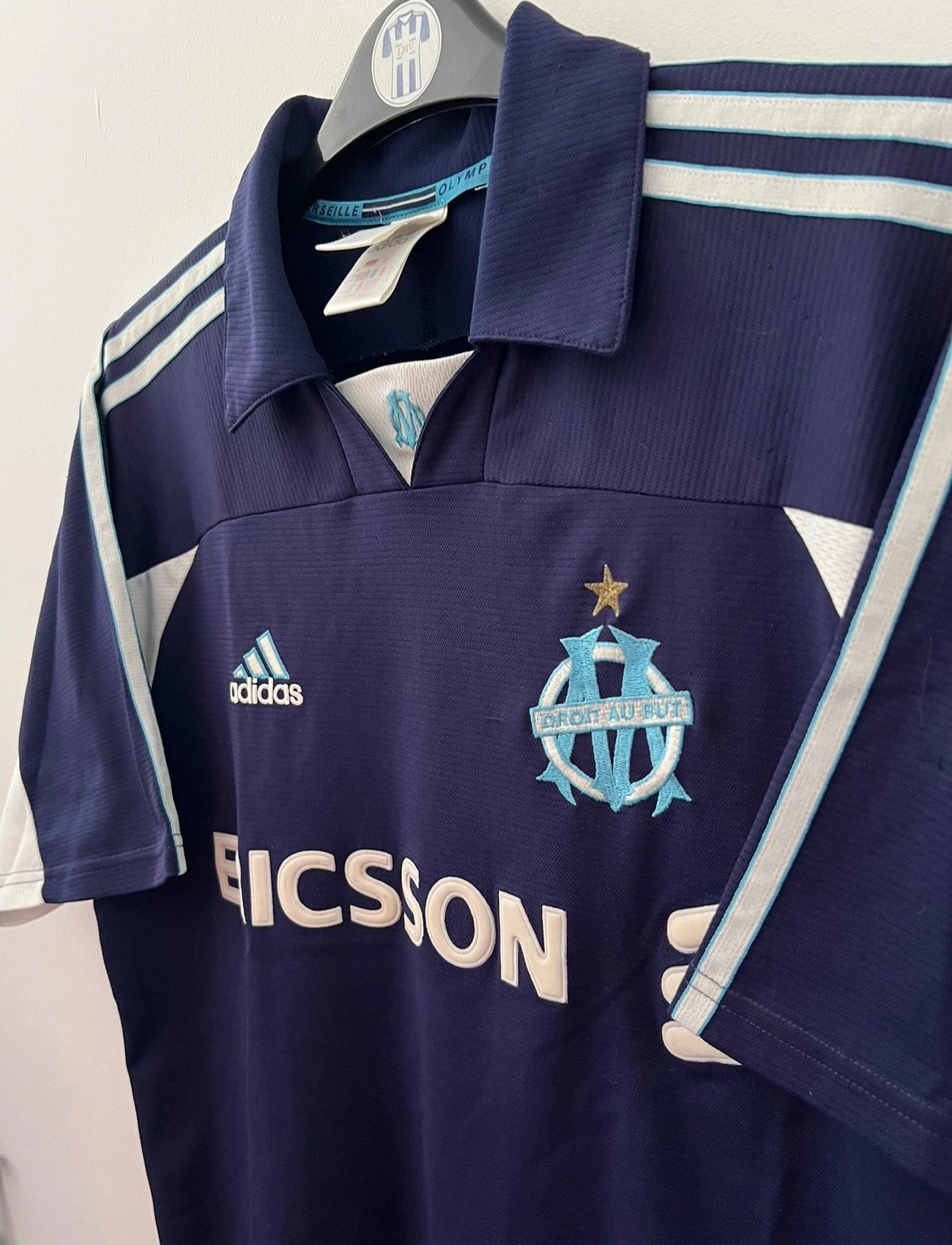 Maillot de foot vintage OM 1999/2000 extérieur bleu. On peut retrouver l'équipementier Adidas et le sponsor Ericsson. Il s'agit d'un maillot authentique d'époque.