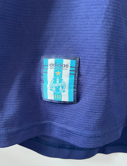 Maillot de foot vintage bleu de l'OM 1999/2000. On peut retrouver l'équipementier Adidas et le sponsor Ericsson. Il s'agit d'un maillot authentique d'époque.