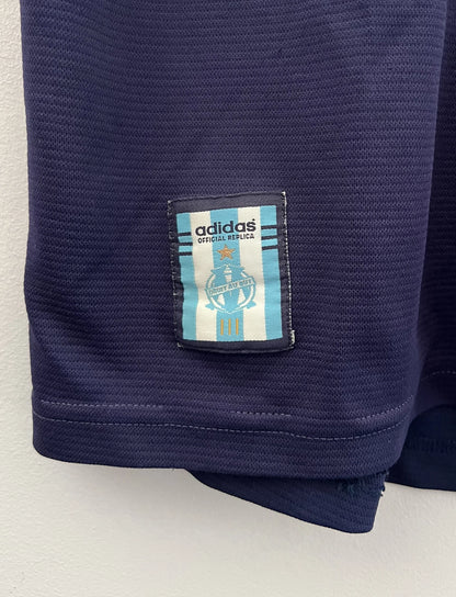 Maillot de foot vintage OM 1999/2000 extérieur bleu. On peut retrouver l'équipementier Adidas et le sponsor Ericsson. Il s'agit d'un maillot authentique d'époque.