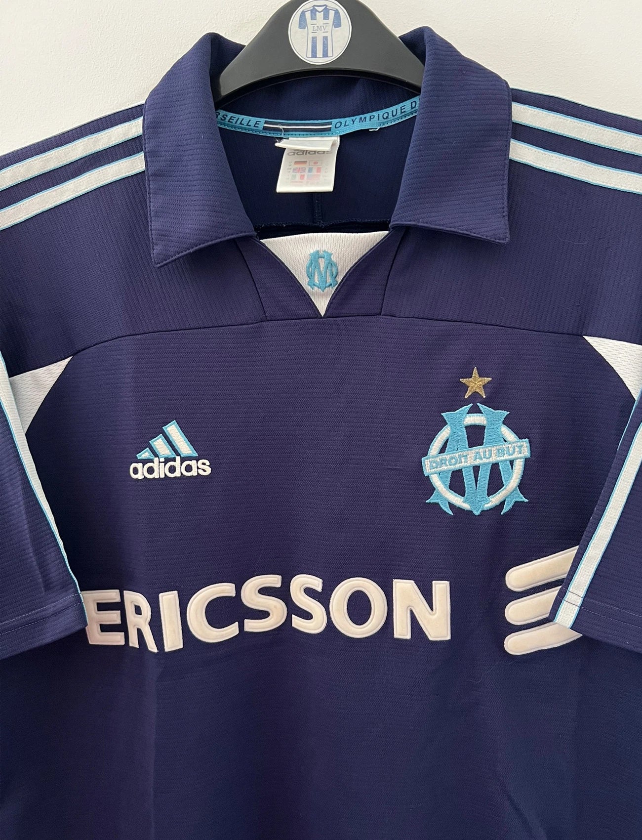 Maillot de foot vintage OM 1999/2000 extérieur bleu. On peut retrouver l'équipementier Adidas et le sponsor Ericsson. Il s'agit d'un maillot authentique d'époque.