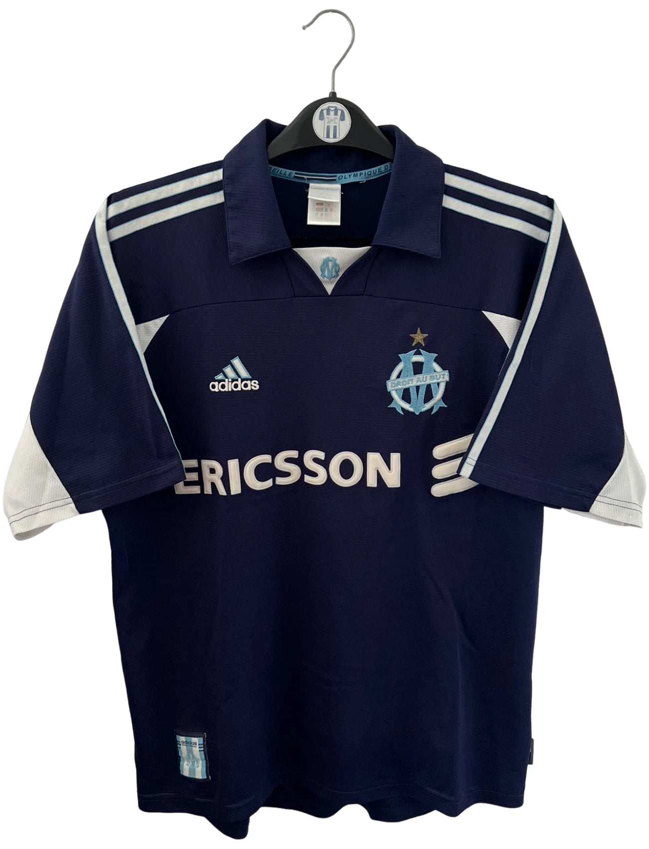 Maillot de foot vintage OM 1999/2000 extérieur bleu. On peut retrouver l'équipementier Adidas et le sponsor Ericsson. Il s'agit d'un maillot authentique d'époque.