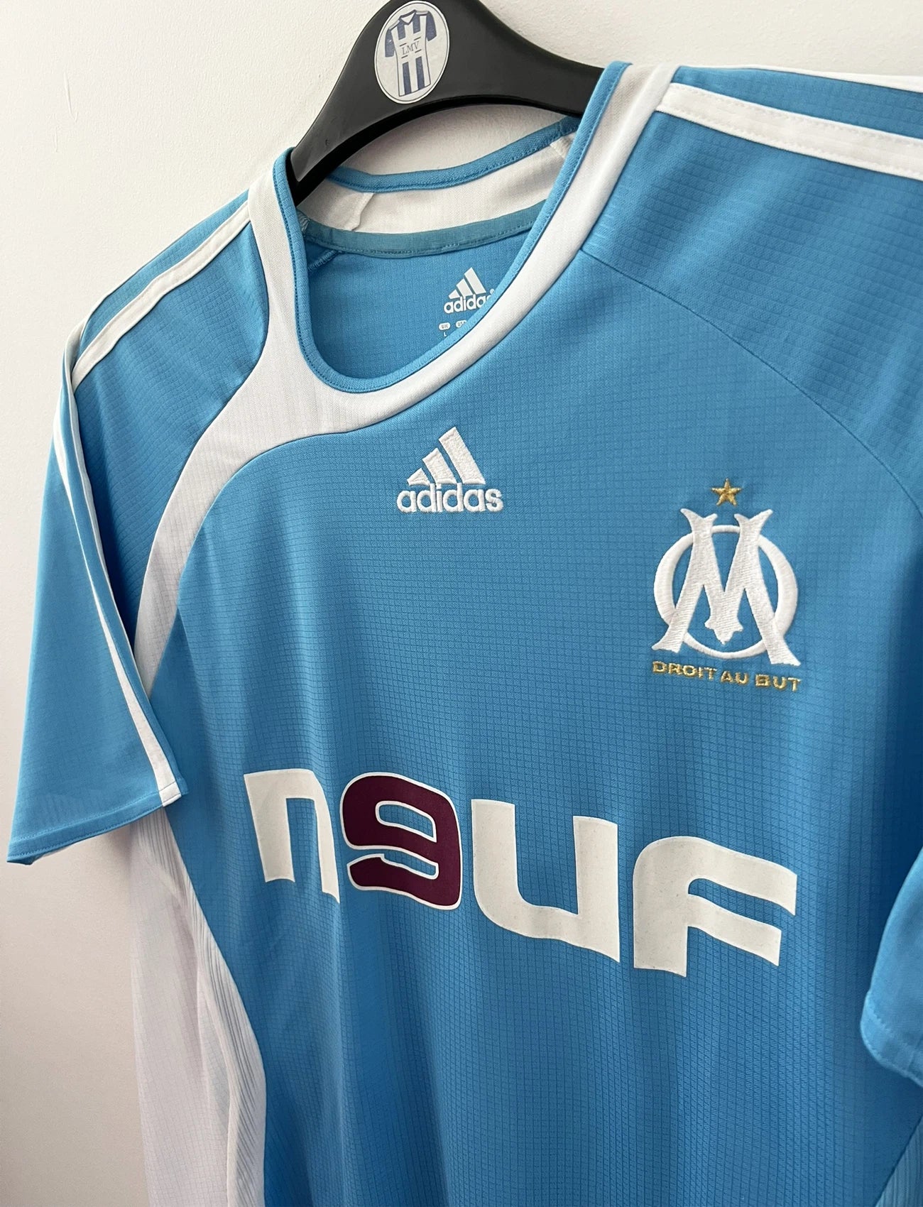 Maillot de foot vintage extérieur bleu et blanc de l'OM 2006/2007. On peut retrouver l'équipementier Adidas et le sponsor Neuf. Le maillot est floqué du numéro 7 Franck Ribery. Il s'agit d'un maillot authentique d'époque.