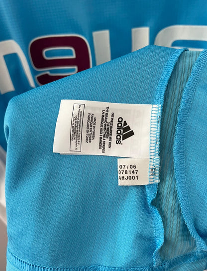 Maillot de foot vintage extérieur bleu et blanc de l'OM 2006/2007. On peut retrouver l'équipementier Adidas et le sponsor Neuf. Le maillot est floqué du numéro 7 Franck Ribery. Il s'agit d'un maillot authentique d'époque.