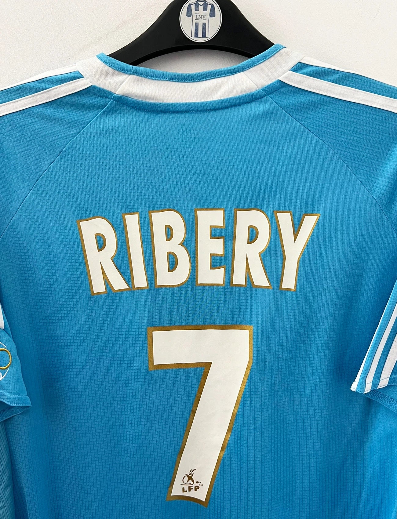 Maillot de foot vintage extérieur bleu et blanc de l'OM 2006/2007. On peut retrouver l'équipementier Adidas et le sponsor Neuf. Le maillot est floqué du numéro 7 Franck Ribery. Il s'agit d'un maillot authentique d'époque.