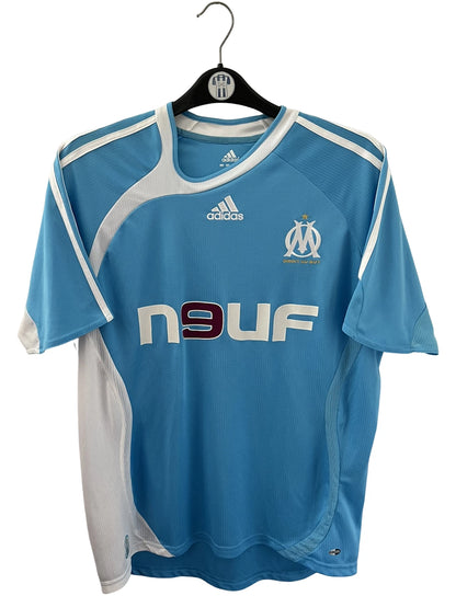 Maillot de foot vintage extérieur bleu et blanc de l'OM 2006/2007. On peut retrouver l'équipementier Adidas et le sponsor Neuf. Le maillot est floqué du numéro 7 Franck Ribery. Il s'agit d'un maillot authentique d'époque.
