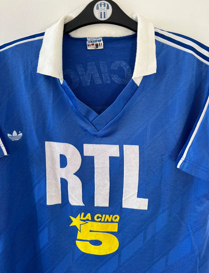 Maillot de foot vintage extérieur bleu du PSG saison 1988/1989. On peut retrouver l'équipementier Adidas et le sponsor RTL, La Cinq et Canal +. Il s'agit d'un maillot authentique d'époque.