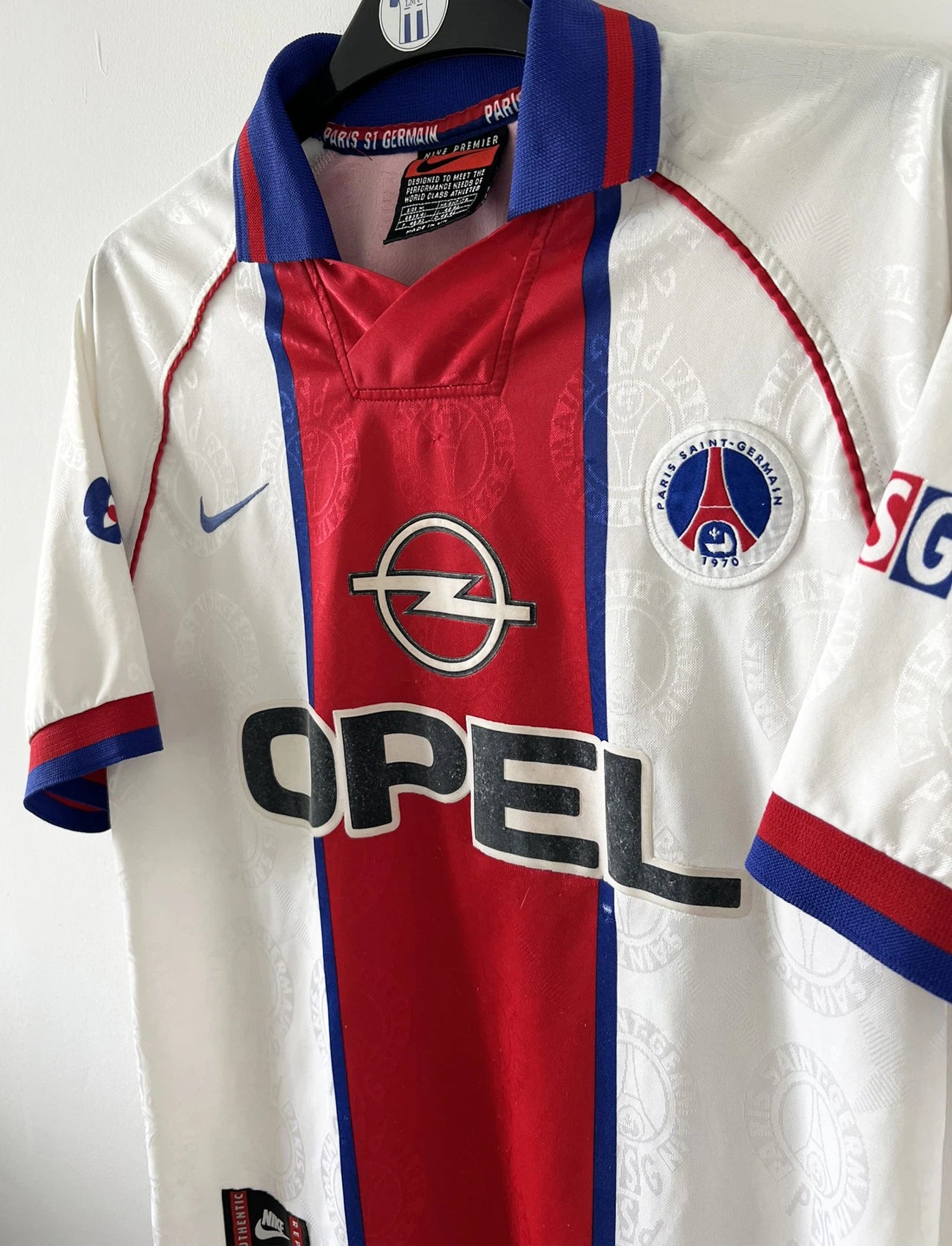 Maillot de foot vintage blanc rouge et bleu du PSG de la saison 1996/1997. On peut retrouver l'équipementier nike et le sponsor opel. Il s'agit d'un maillot authentique d'époque.
