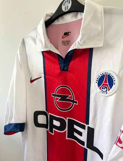 Maillot extérieur PSG blanc et rouge de la saison 1998/1999. On peut retrouver l'équipementier Nike et le sponsor Opel. Il s'agit d'un maillot authentique d'époque.