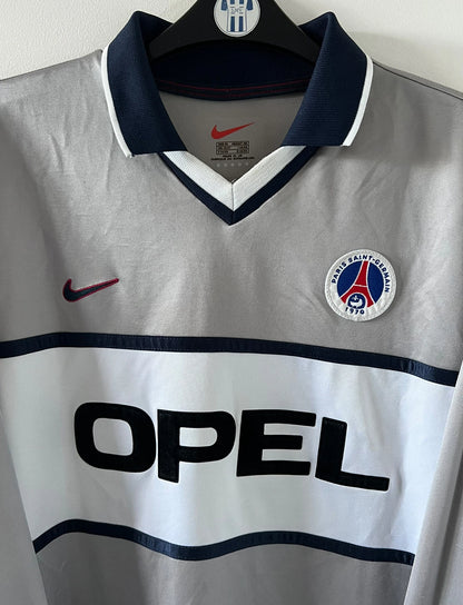 Maillot de foot vintage domicile gris du PSG de la saison 2000/2001. On peut retrouver l'équipementier Nike et le sponsor Opel. Il s'agit d'un maillot authentique d'époque, issu du stock pro du PSG.