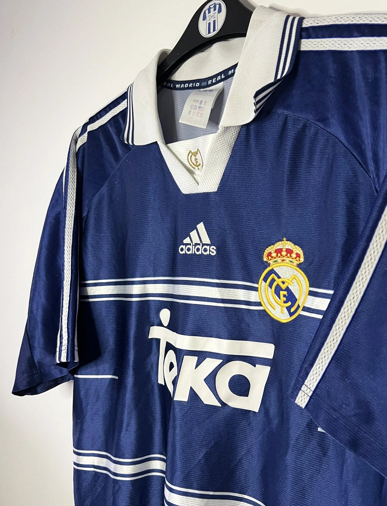 Maillot de foot vintage extérieur bleu du Real Madrid de la saison 1998/1999. On peut retrouver l'équipementier Adidas et le sponsor Teka. Il s'agit d'un maillot authentique d'époque.