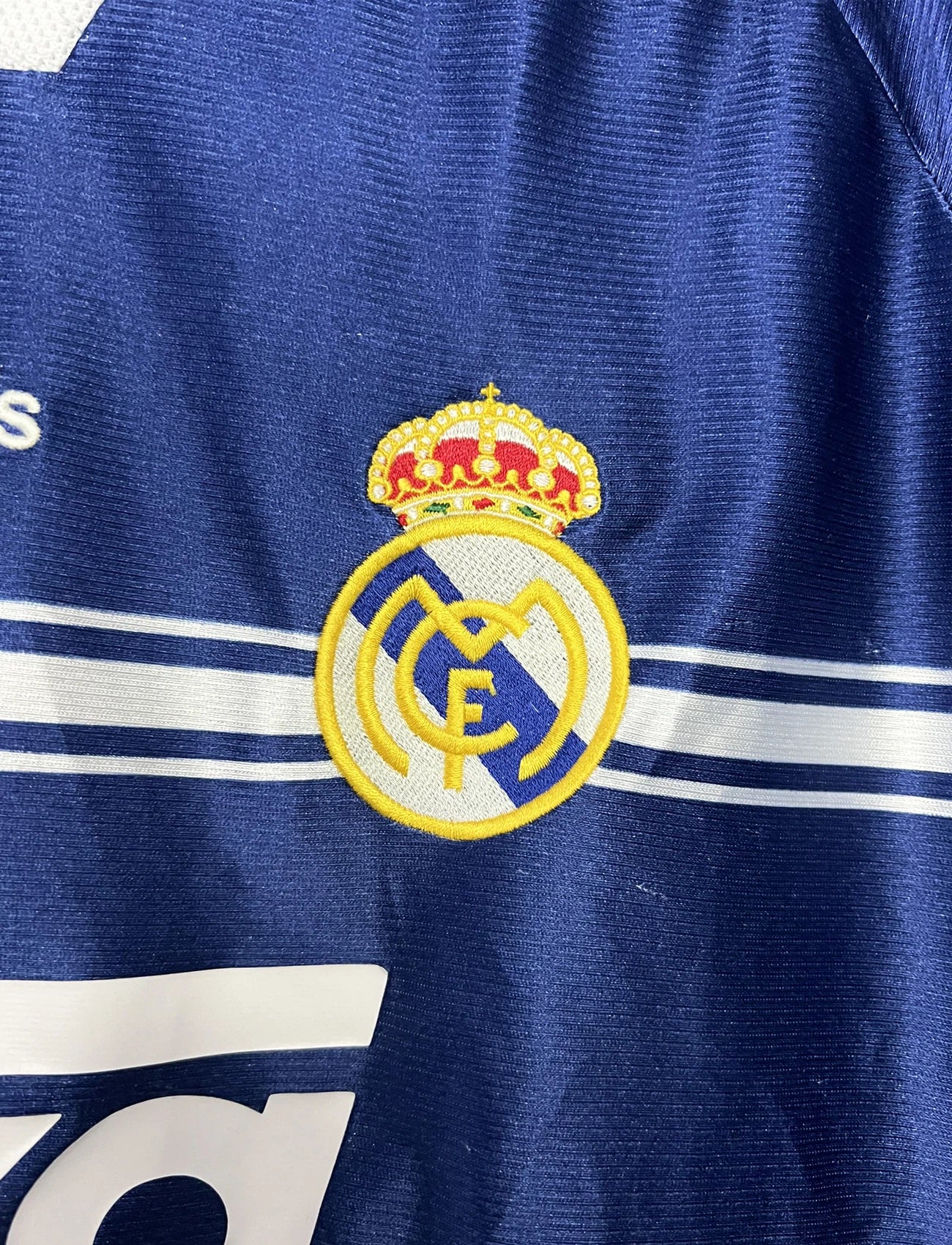 Maillot de foot vintage extérieur bleu du Real Madrid de la saison 1998/1999. On peut retrouver l'équipementier Adidas et le sponsor Teka. Il s'agit d'un maillot authentique d'époque.