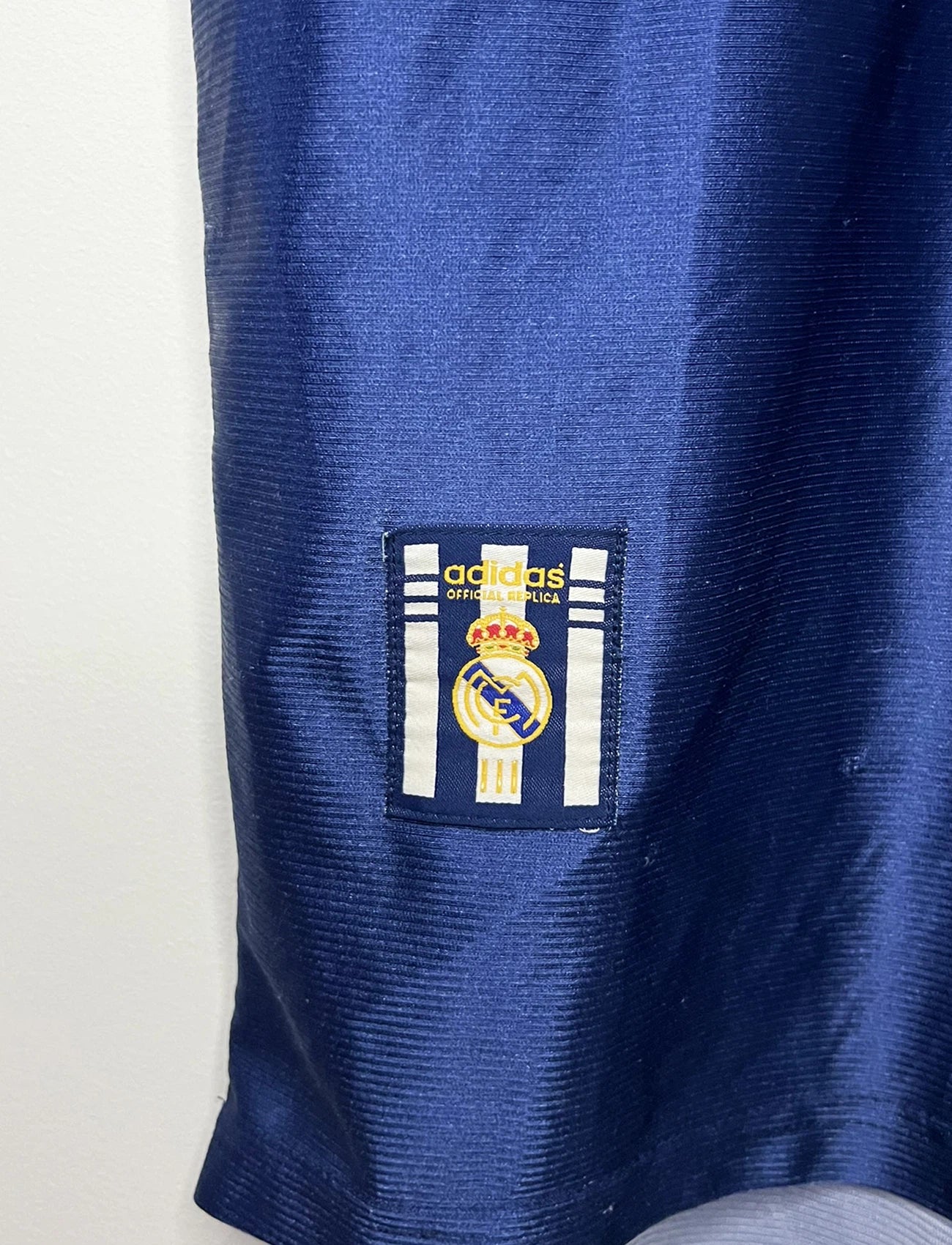 Maillot de foot vintage extérieur bleu du Real Madrid de la saison 1998/1999. On peut retrouver l'équipementier Adidas et le sponsor Teka. Il s'agit d'un maillot authentique d'époque.