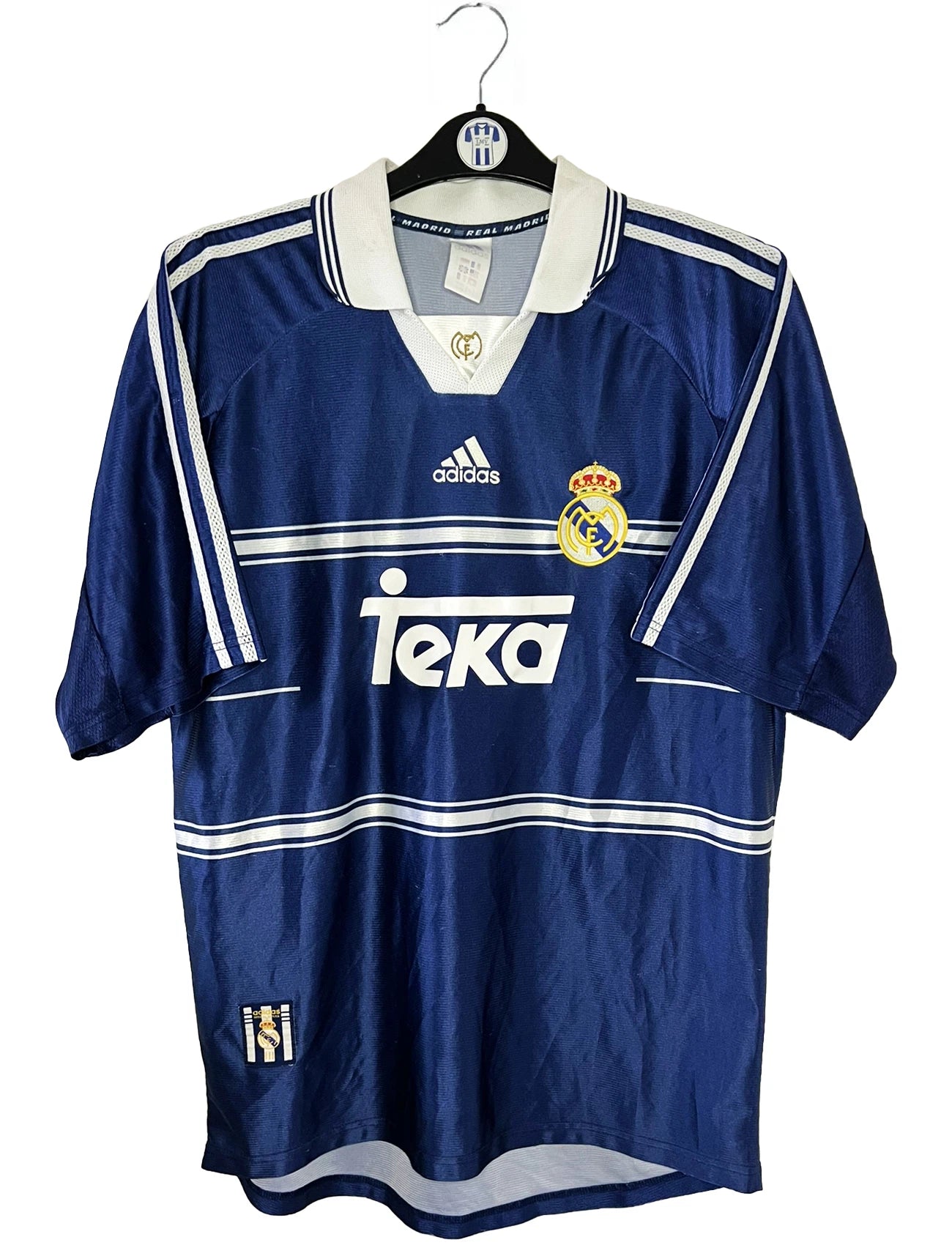 Maillot de foot vintage extérieur bleu du Real Madrid de la saison 1998/1999. On peut retrouver l'équipementier Adidas et le sponsor Teka. Il s'agit d'un maillot authentique d'époque.