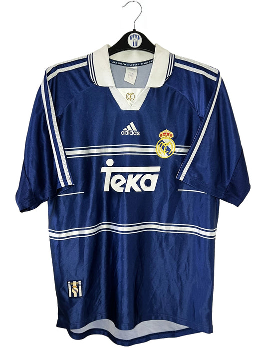 Maillot de foot vintage extérieur bleu du Real Madrid de la saison 1998/1999. On peut retrouver l'équipementier Adidas et le sponsor Teka. Il s'agit d'un maillot authentique d'époque.