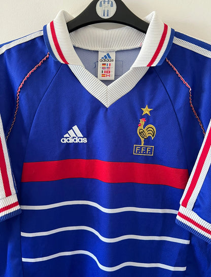 Maillot foot vintage domicile equipe de france 1998 bleu blanc et rouge. On peut retrouver l'équipementier adidas. Il s'agit d'un maillot authentique d'époque. Le maillot est floqué du numéro 10 Zinedine Zidane et comporte également sa signature avec la mention "pour toi Zinedine Zidane"