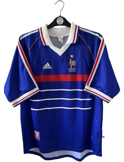 Maillot foot vintage domicile equipe de france 1998 bleu blanc et rouge. On peut retrouver l'équipementier adidas. Il s'agit d'un maillot authentique d'époque. Le maillot est floqué du numéro 10 Zinedine Zidane et comporte également sa signature avec la mention "pour toi Zinedine Zidane"