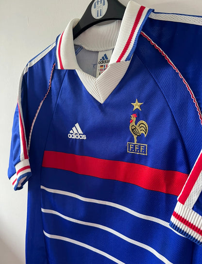 Maillot foot vintage domicile equipe de france 1998 bleu blanc et rouge. On peut retrouver l'équipementier adidas. Il s'agit d'un maillot authentique d'époque. Le maillot est floqué du numéro 10 Zinedine Zidane et comporte également sa signature avec la mention "pour toi Zinedine Zidane"