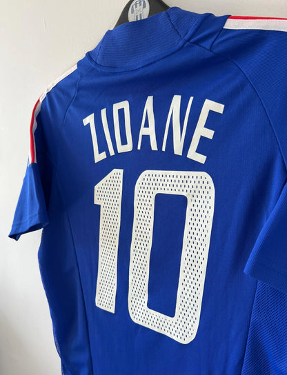 Maillot de foot vintage domicile bleu de l'équipe de france 2002. On peut retrouver l'équipementier Adidas et le flocage de Zidane. Il s'agit d'un maillot authentique d'époque.