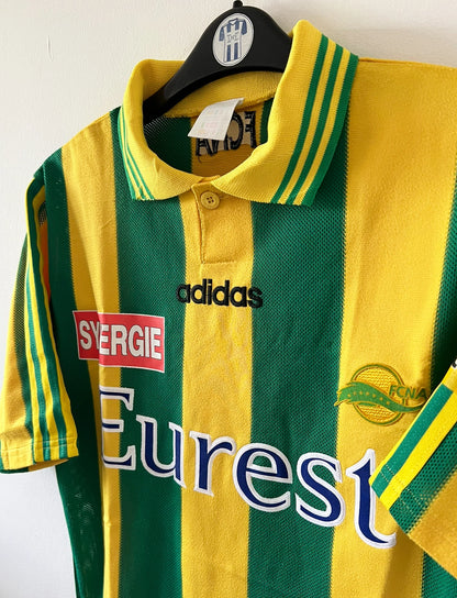 Maillot de foot vintage domicile jaune et vert du FC Nantes 1996/1997. On peut retrouver l'équipementier Adidas et le sponsor Eurest et Playstation. Il s'agit d'un maillot authentique d'époque.