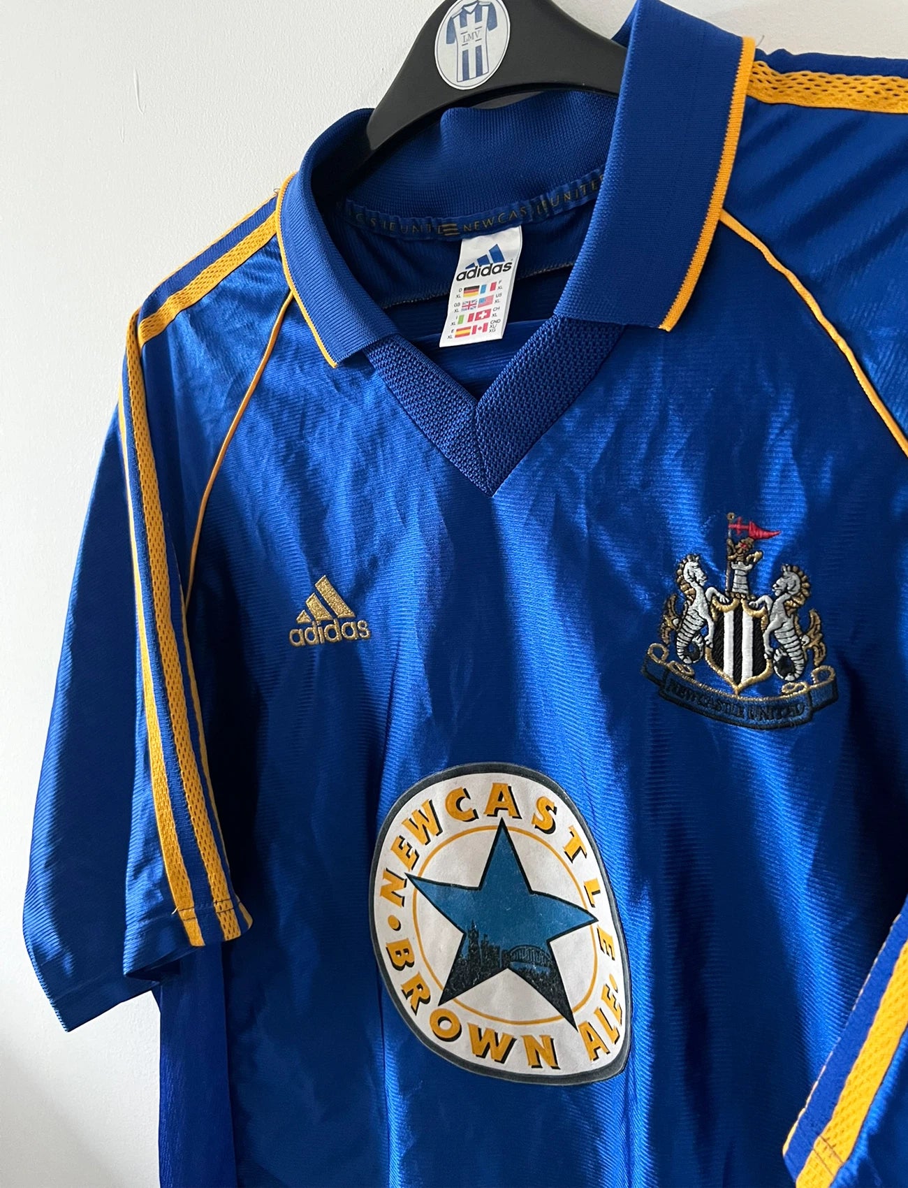 Maillot de foot vintage extérieur bleu de Newcastle 1998/1999. On peut retrouver l'équipementier Adidas et le sponsor Newcastle Brown Ale. Il s'agit d'un maillot authentique d'époque.