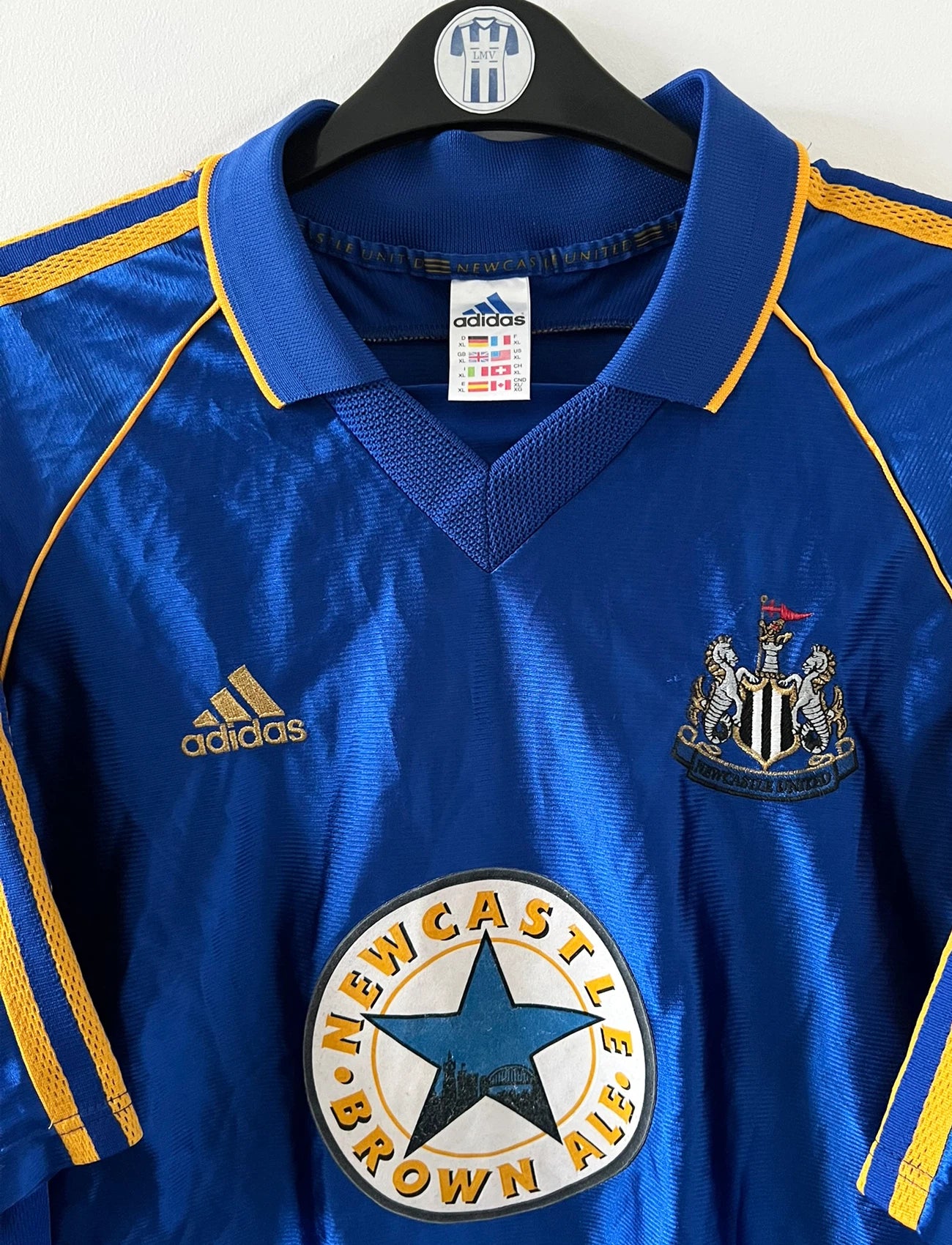 Maillot de foot vintage extérieur bleu de Newcastle 1998/1999. On peut retrouver l'équipementier Adidas et le sponsor Newcastle Brown Ale. Il s'agit d'un maillot authentique d'époque.