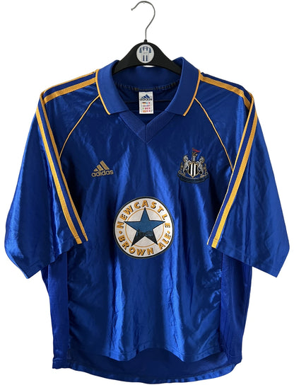 Maillot de foot vintage extérieur bleu de Newcastle 1998/1999. On peut retrouver l'équipementier Adidas et le sponsor Newcastle Brown Ale. Il s'agit d'un maillot authentique d'époque.