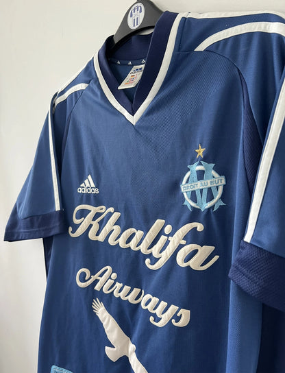 Maillot de foot vintage domicile de l'OM de la saison 2001-2002. Le maillot est de couleur bleu et blanc. On peut retrouver l'équipementier adidas et le sponsor khalifa airways. Il s'agit d'un maillot authentique d'époque comportant les numéros 699635