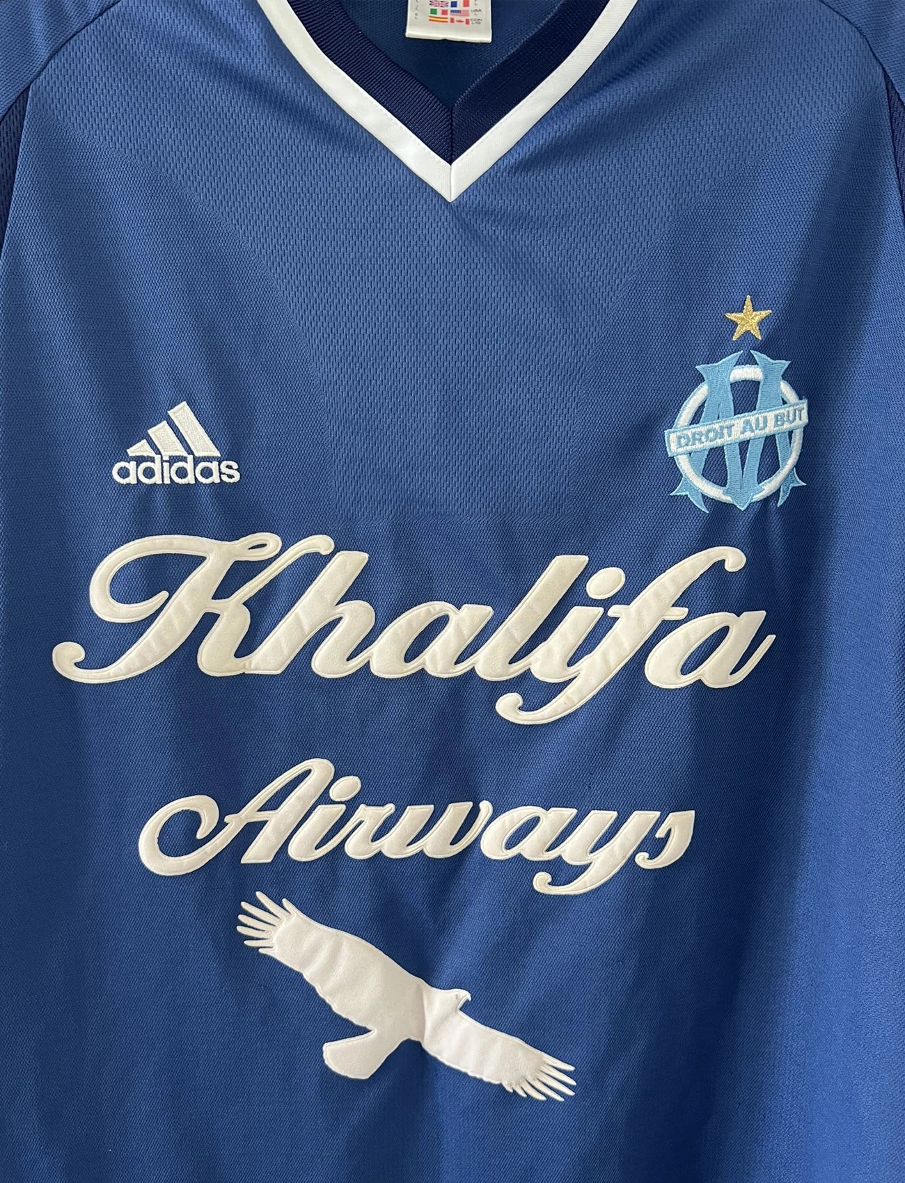 Maillot de foot vintage domicile de l'OM de la saison 2001-2002. Le maillot est de couleur bleu et blanc. On peut retrouver l'équipementier adidas et le sponsor khalifa airways. Il s'agit d'un maillot authentique d'époque comportant les numéros 699635