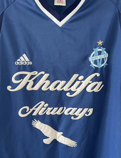 Maillot de foot vintage domicile de l'OM de la saison 2001-2002. Le maillot est de couleur bleu et blanc. On peut retrouver l'équipementier adidas et le sponsor khalifa airways. Il s'agit d'un maillot authentique d'époque comportant les numéros 699635