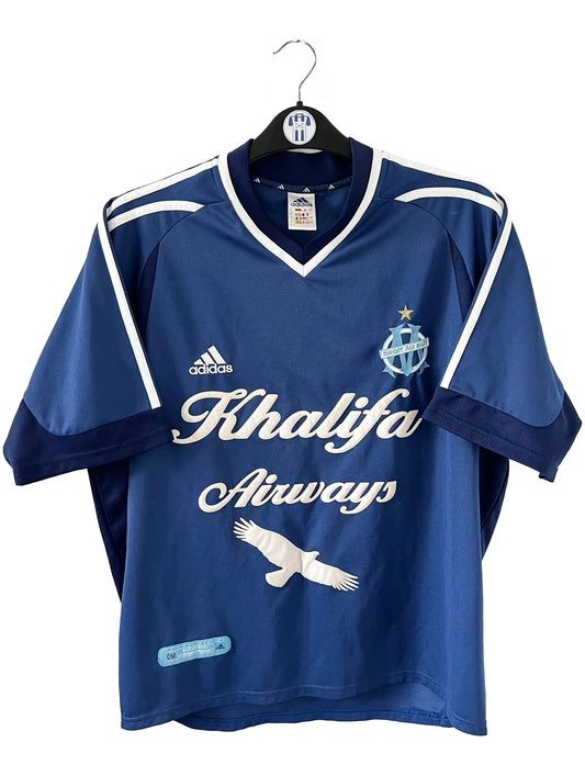 Maillot de foot vintage domicile de l'OM de la saison 2001-2002. Le maillot est de couleur bleu et blanc. On peut retrouver l'équipementier adidas et le sponsor khalifa airways. Il s'agit d'un maillot authentique d'époque comportant les numéros 699635