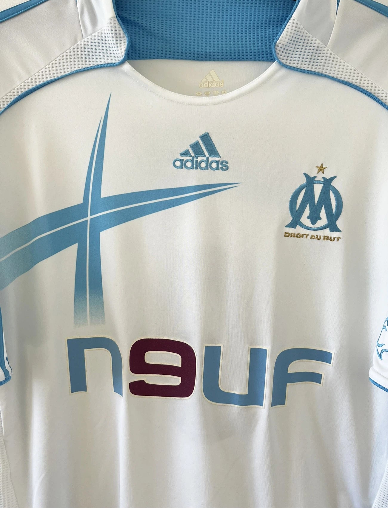 Maillot de foot vintage domicile de l'OM de la saison 2006/2007. Le maillot est de couleur blanc et bleu. On peut retrouver l'équipementier adidas et le sponsor Neuf. Le maillot est floqué du numéro 9 Djibril Cissé. Il s'agit d'un maillot authentique d'époque comportant les numéros 084929