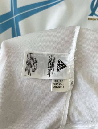 Maillot de foot vintage domicile de l'OM de la saison 2006/2007. Le maillot est de couleur blanc et bleu. On peut retrouver l'équipementier adidas et le sponsor Neuf. Le maillot est floqué du numéro 9 Djibril Cissé. Il s'agit d'un maillot authentique d'époque comportant les numéros 084929