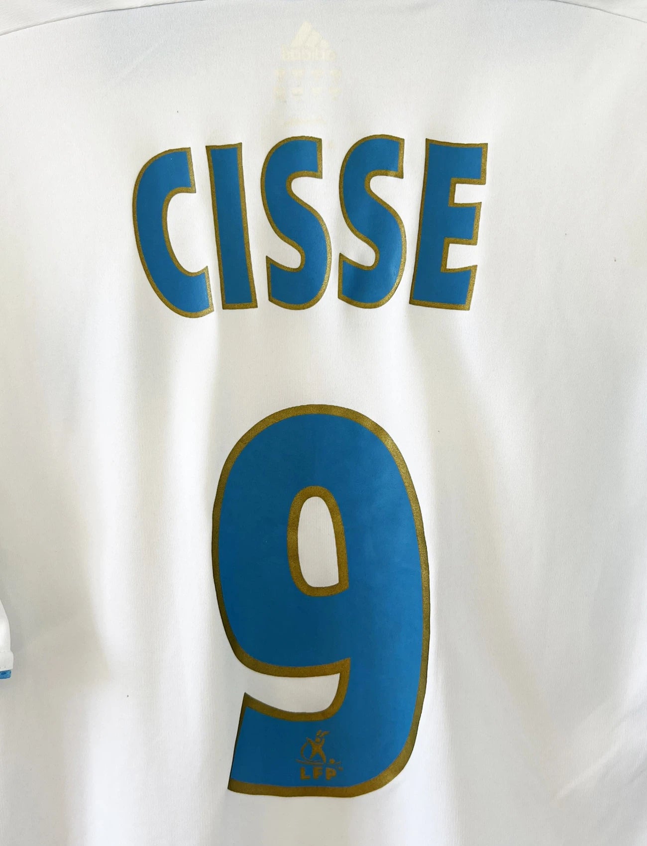 Maillot de foot vintage domicile de l'OM de la saison 2006/2007. Le maillot est de couleur blanc et bleu. On peut retrouver l'équipementier adidas et le sponsor Neuf. Le maillot est floqué du numéro 9 Djibril Cissé. Il s'agit d'un maillot authentique d'époque comportant les numéros 084929