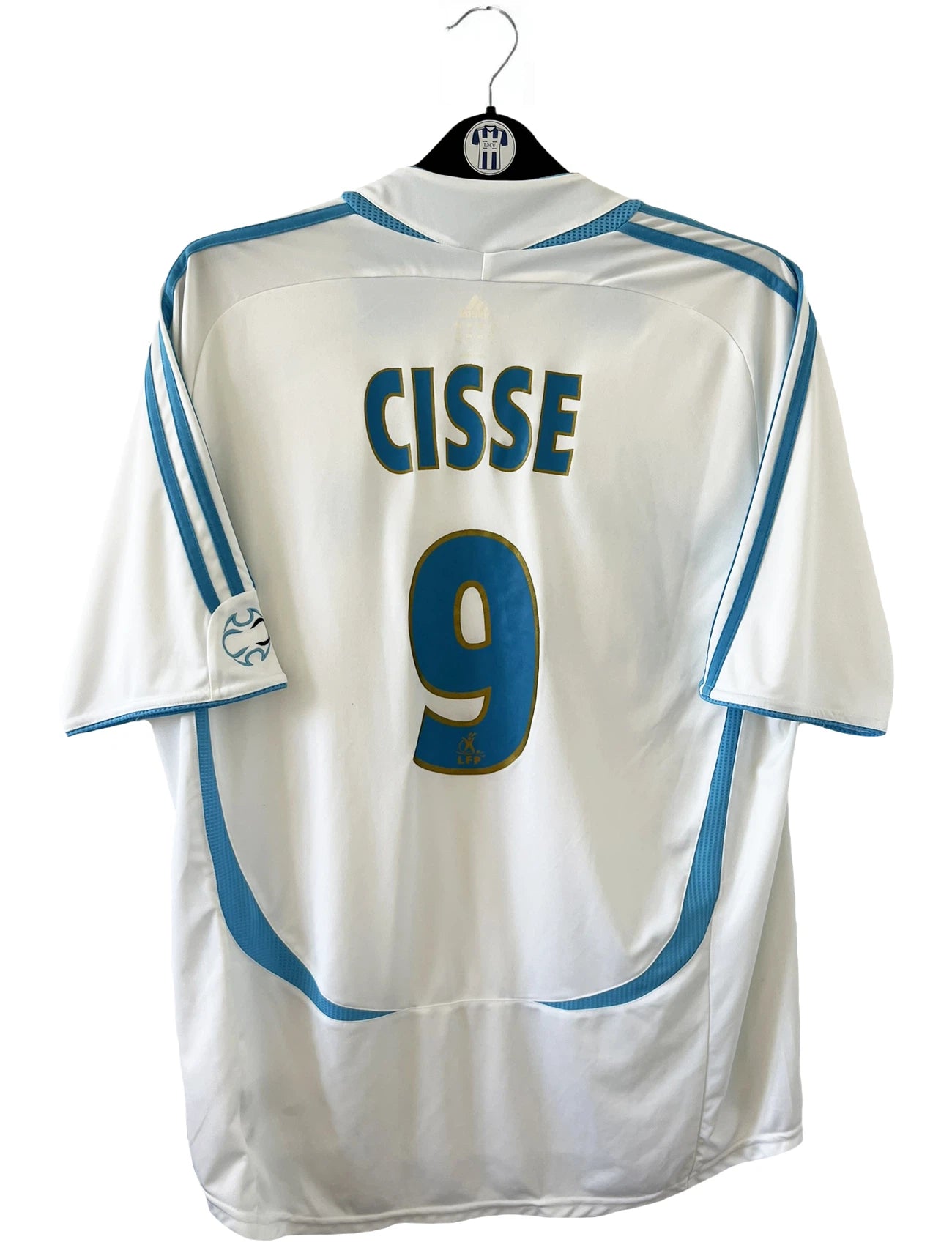 Maillot de foot vintage domicile de l'OM de la saison 2006/2007. Le maillot est de couleur blanc et bleu. On peut retrouver l'équipementier adidas et le sponsor Neuf. Le maillot est floqué du numéro 9 Djibril Cissé. Il s'agit d'un maillot authentique d'époque comportant les numéros 084929