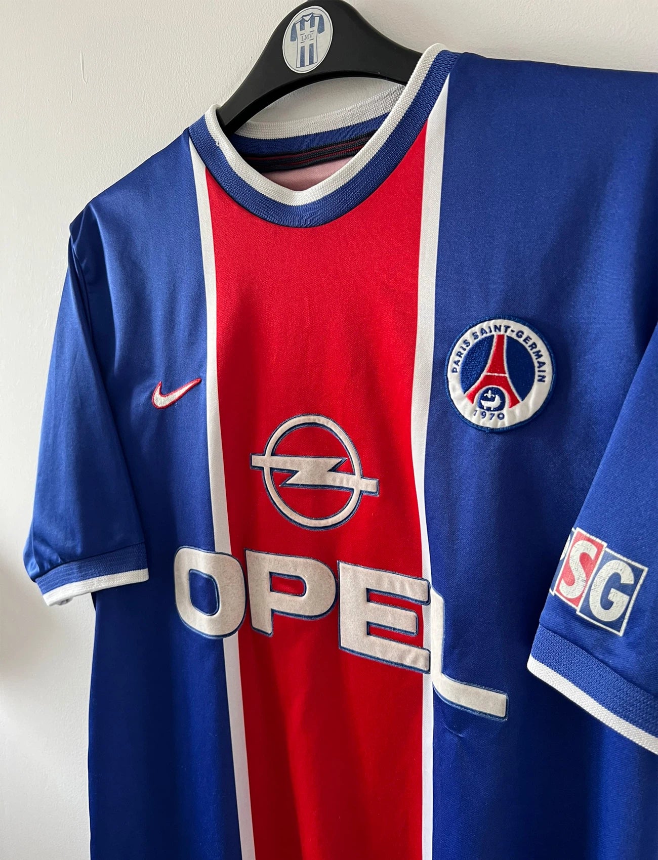 Maillot de foot vintage domicile rouge et bleu du PSG 1999/2000. On peut retrouver l'équipementier Nike et le sponsor Opel. Il s'agit d'un maillot authentique d'époque.