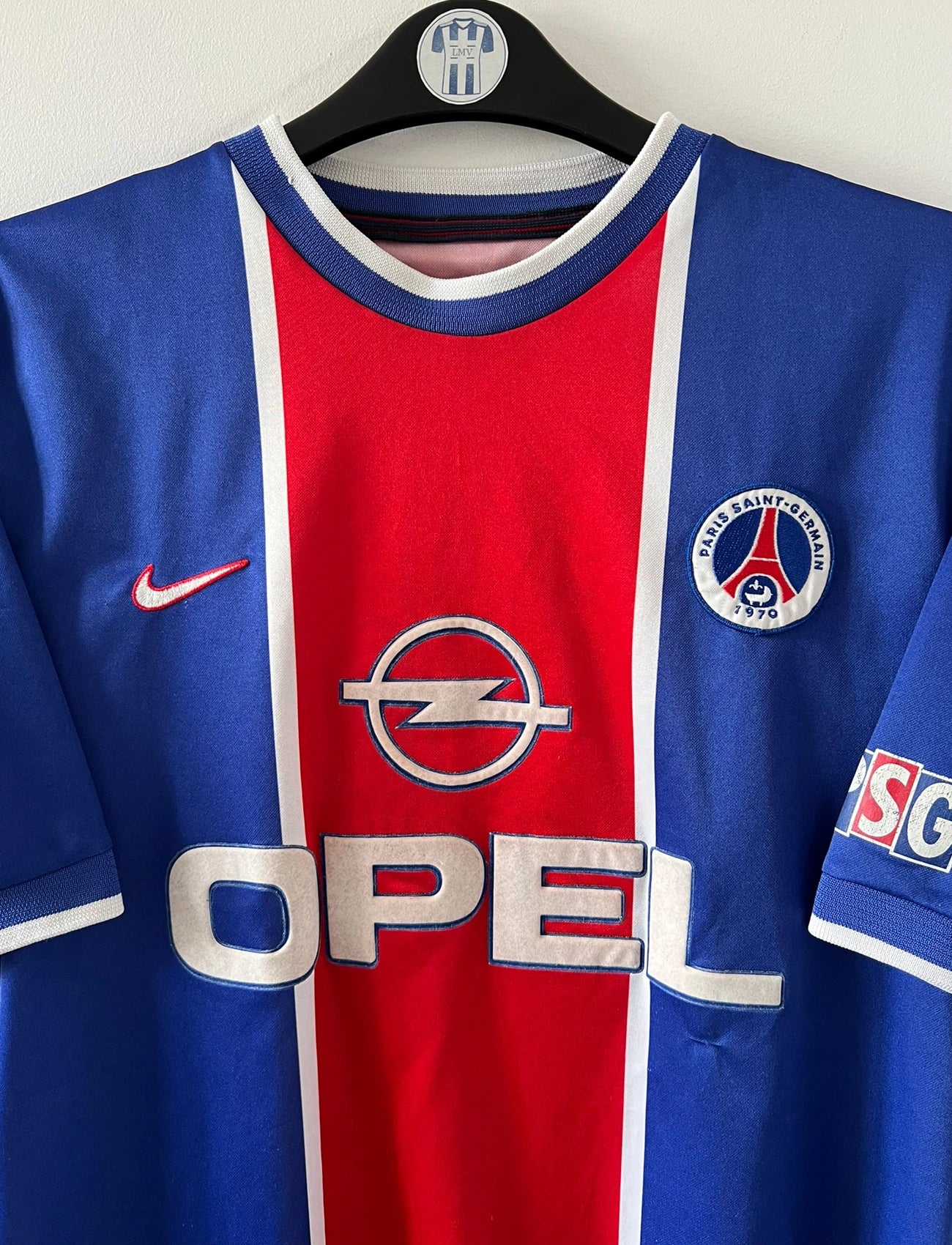 Maillot de foot vintage domicile rouge et bleu du PSG 1999/2000. On peut retrouver l'équipementier Nike et le sponsor Opel. Il s'agit d'un maillot authentique d'époque.