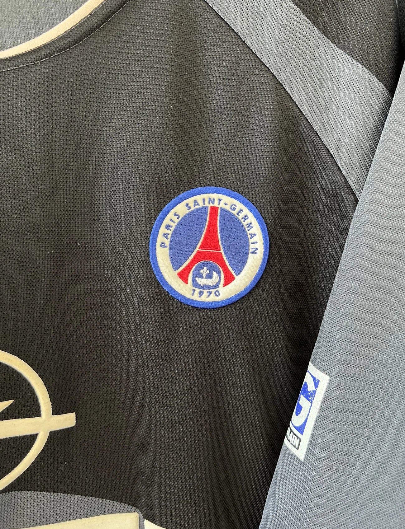 Maillot de foot vintage third du PSG de la saison 2001/2002. Le maillot est de couleur noir et gris. On peut retrouver l'équipementier nike et le sponsor Opel. Le maillot est floqué du numéro 21 Ronaldinho. Le maillot possède l'étiquette avec les numéros F1 ORX. Il s'agit d'un maillot authentique d'époque.