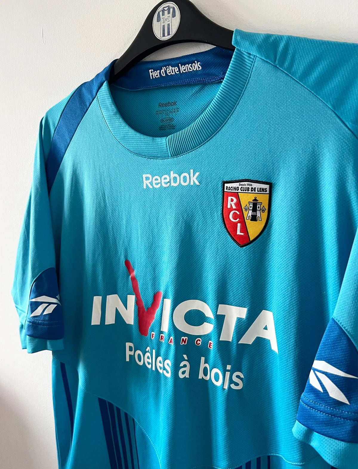 Maillot de foot vintage extérieur bleu du RC Lens 2009/2010. On peut retrouver l'équipementier Reebok et le sponsor Invicta. Il s'agit d'un maillot authentique d'époque.