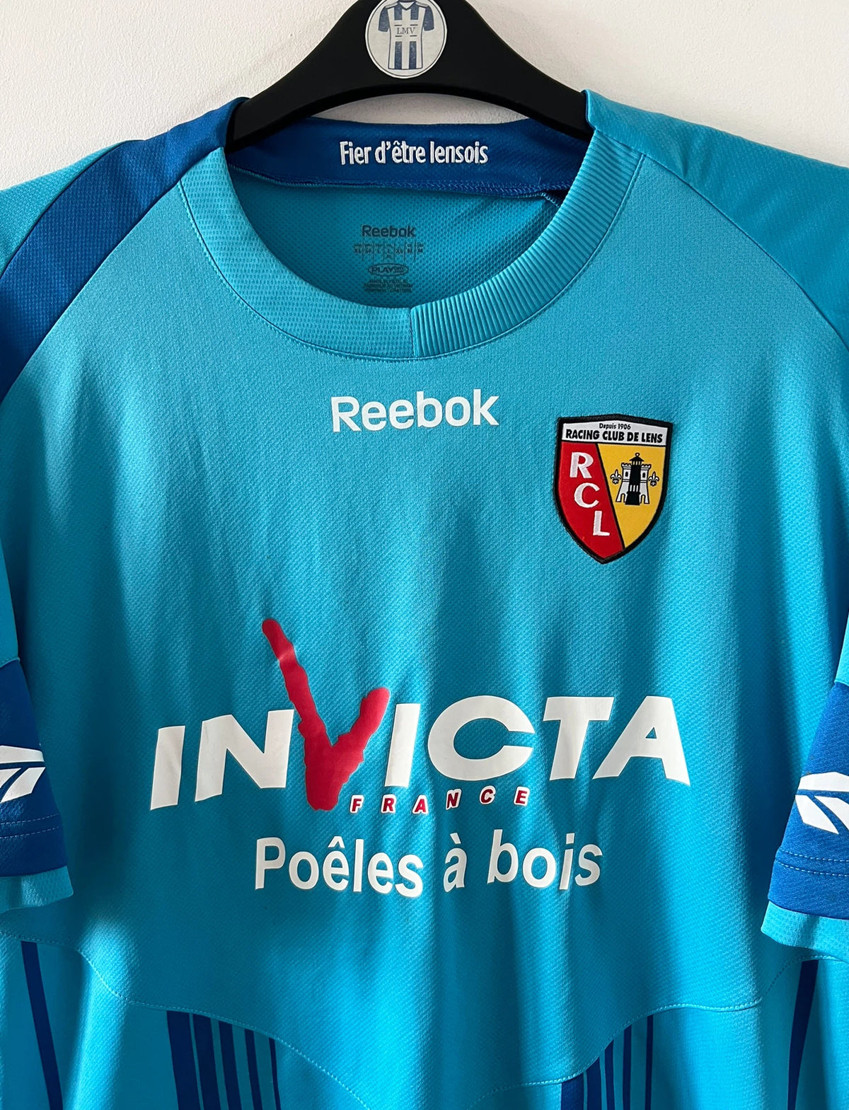 Maillot de foot vintage extérieur bleu du RC Lens 2009/2010. On peut retrouver l'équipementier Reebok et le sponsor Invicta. Il s'agit d'un maillot authentique d'époque.