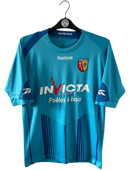 Maillot de foot vintage extérieur bleu du RC Lens 2009/2010. On peut retrouver l'équipementier Reebok et le sponsor Invicta. Il s'agit d'un maillot authentique d'époque.