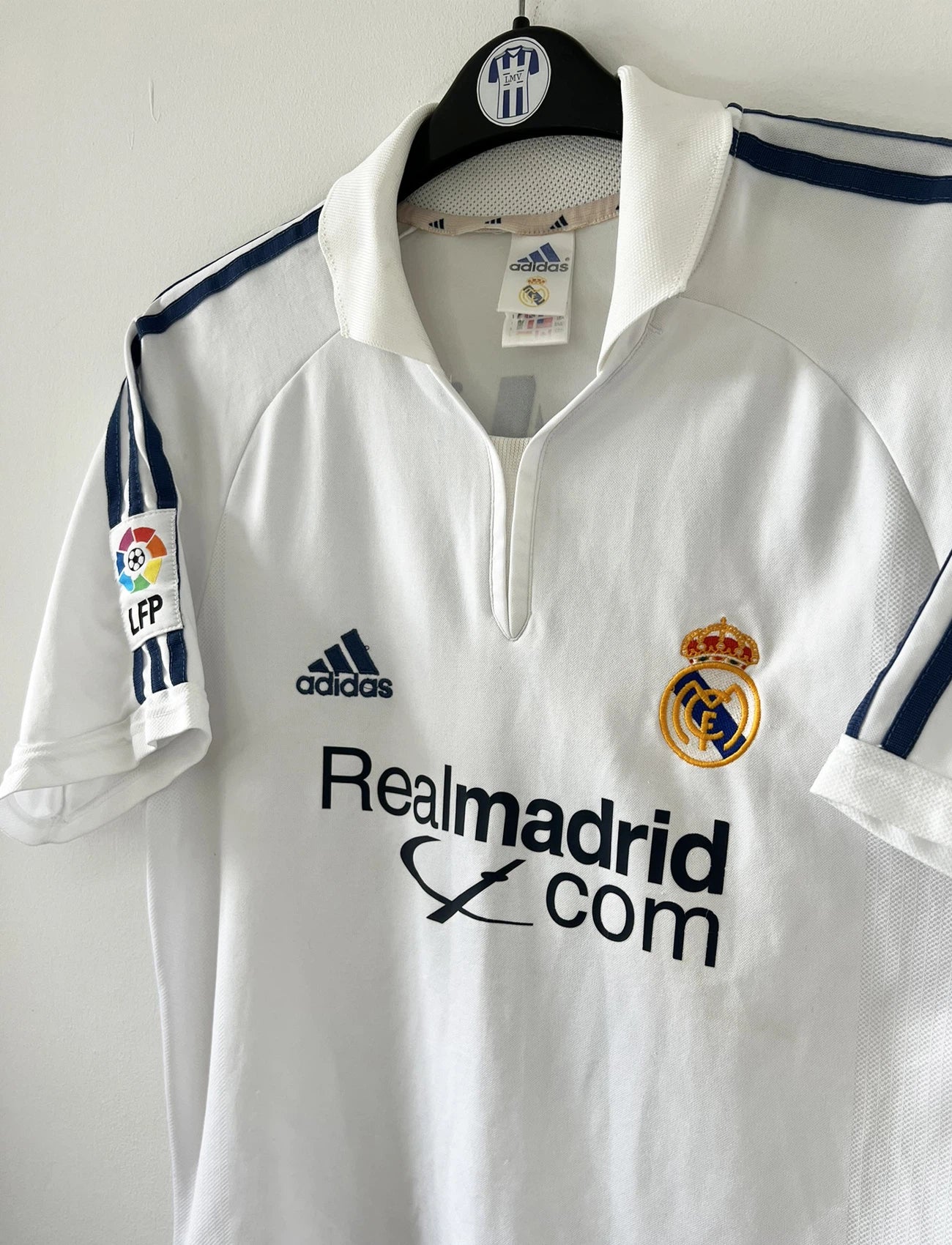 Maillot de foot vintage domicile du real madrid de la saison 2001-2002. Le maillot est de couleur blanc et noir. On peut retrouver l'équipementier adidas et le sponsor Real Madrid.com. Le maillot est floqué du numéro 5 Zinedine Zidane. Il s'agit d'un maillot authentique