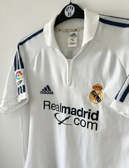 Maillot de foot vintage domicile du real madrid de la saison 2001-2002. Le maillot est de couleur blanc et noir. On peut retrouver l'équipementier adidas et le sponsor Real Madrid.com. Le maillot est floqué du numéro 5 Zinedine Zidane. Il s'agit d'un maillot authentique