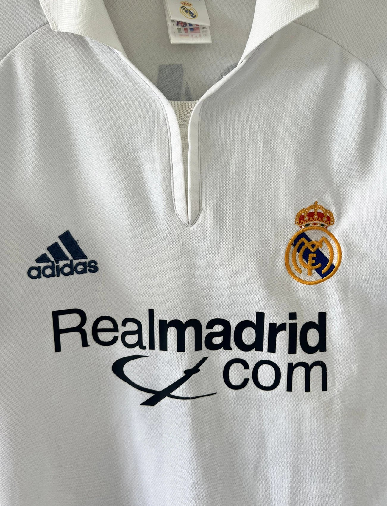 Maillot de foot vintage domicile du real madrid de la saison 2001-2002. Le maillot est de couleur blanc et noir. On peut retrouver l'équipementier adidas et le sponsor Real Madrid.com. Le maillot est floqué du numéro 5 Zinedine Zidane. Il s'agit d'un maillot authentique