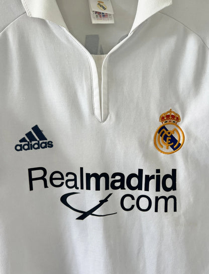 Maillot de foot vintage domicile du real madrid de la saison 2001-2002. Le maillot est de couleur blanc et noir. On peut retrouver l'équipementier adidas et le sponsor Real Madrid.com. Le maillot est floqué du numéro 5 Zinedine Zidane. Il s'agit d'un maillot authentique
