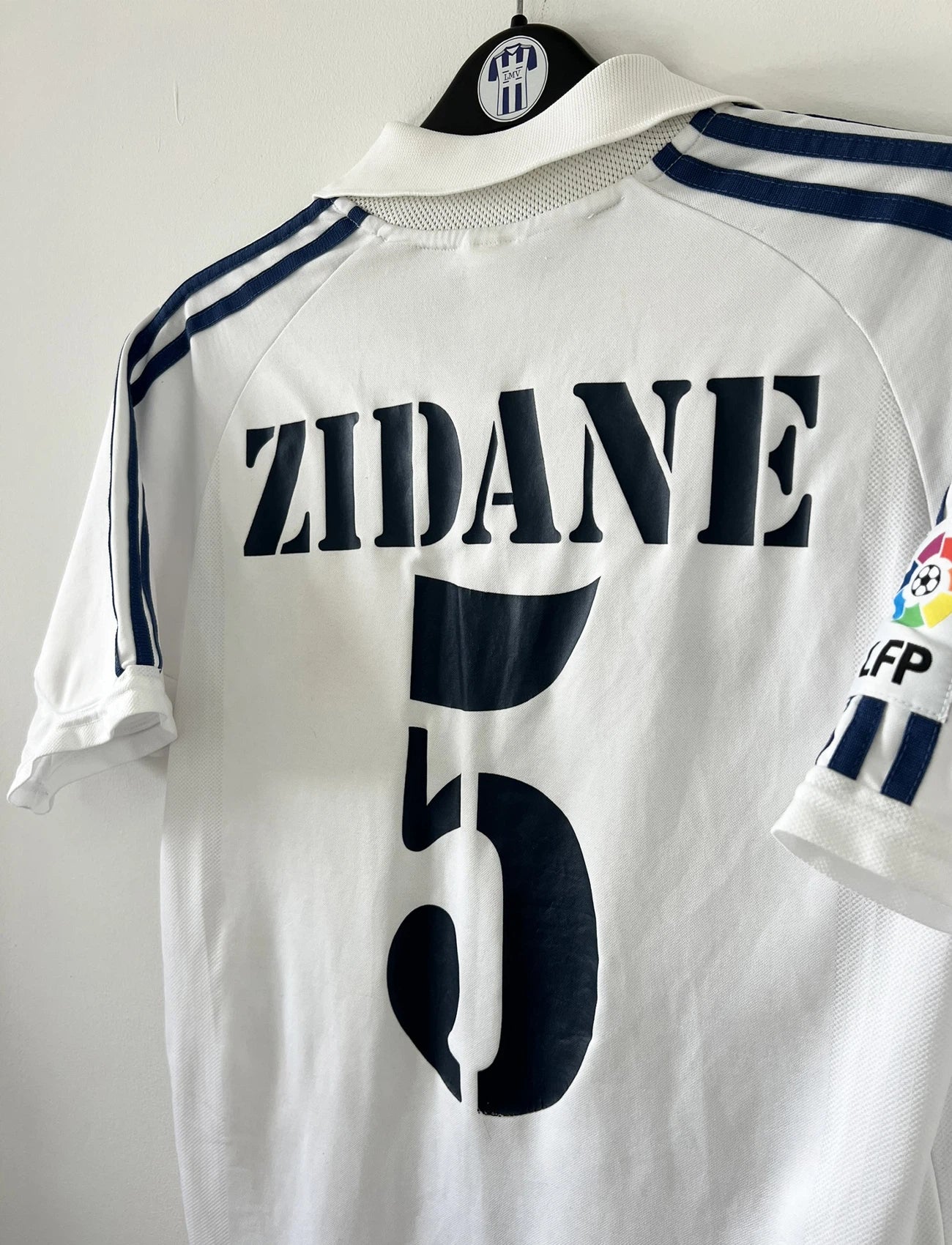 Maillot de foot vintage domicile du real madrid de la saison 2001-2002. Le maillot est de couleur blanc et noir. On peut retrouver l'équipementier adidas et le sponsor Real Madrid.com. Le maillot est floqué du numéro 5 Zinedine Zidane. Il s'agit d'un maillot authentique